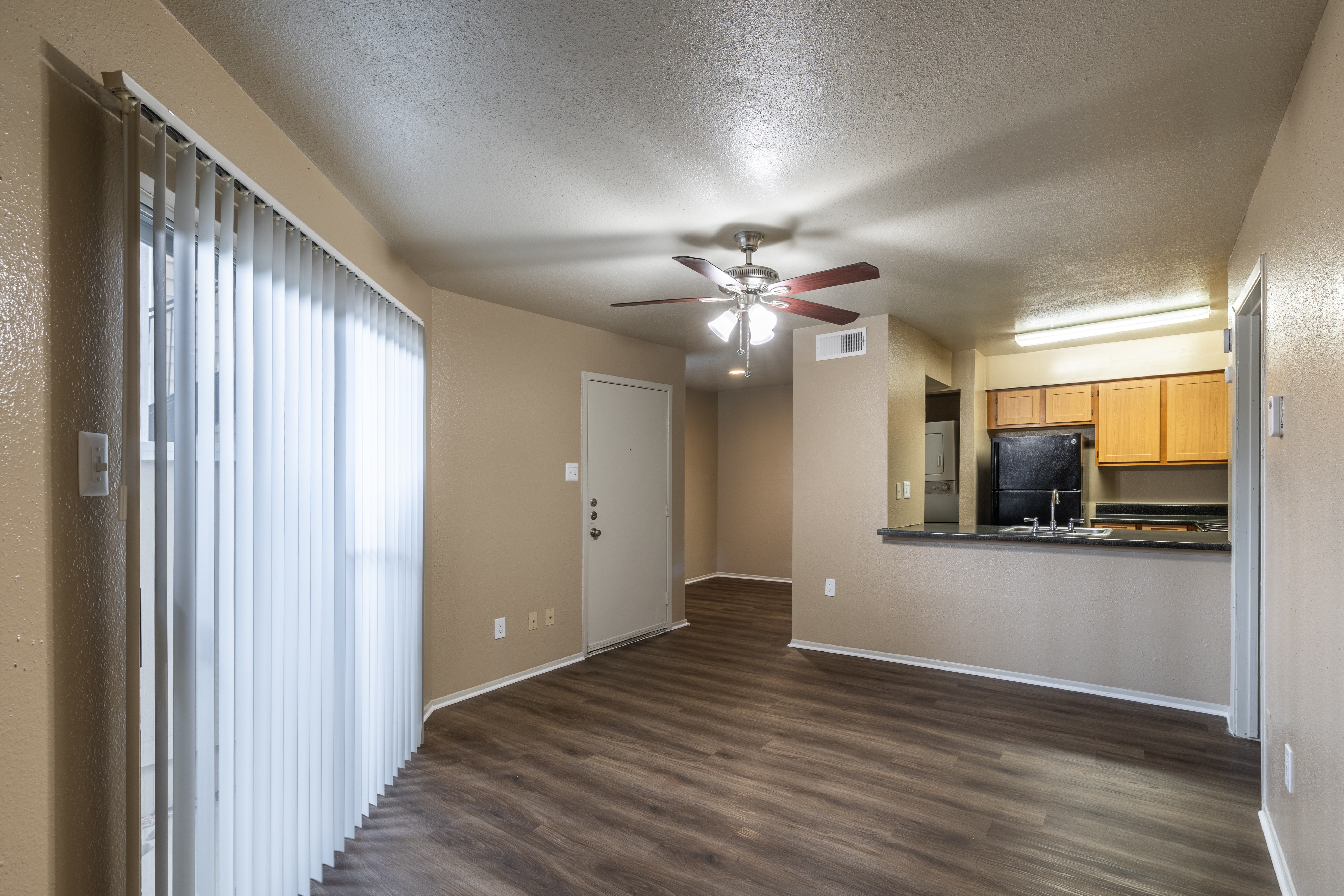 A room with a ceiling fan and a kitchenette in the background.